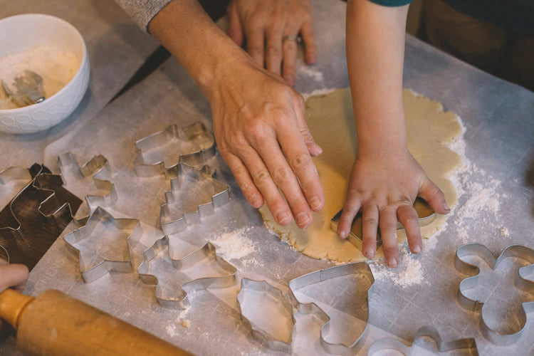 Hands rolling out dough with festive cookie cutters, ideal for baking cookies and holiday treats.